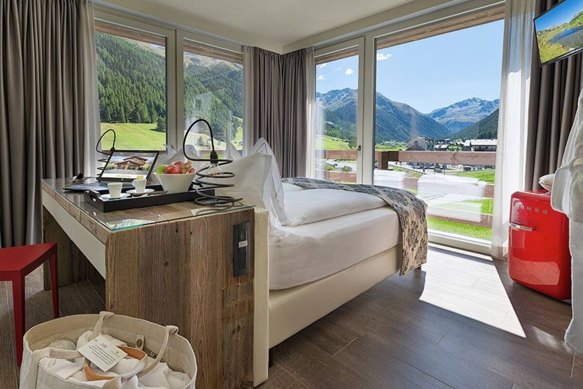 A room with a bed, a desk, a chair, and a view of mountains.