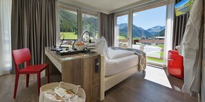 A room with a bed, a desk, a chair, and a view of mountains. - Hotel Sporting - Family Hospitality (Livigno)