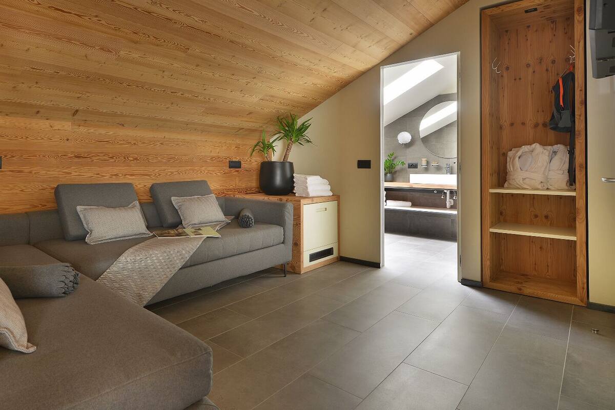A modern living room with a wooden ceiling, a grey sofa, a side table with a plant, and a view into a bathroom.
