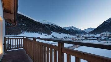 Un balcone con ringhiera in legno che si affaccia su un paesaggio montano innevato e un piccolo paese.