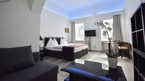 A modern hotel room with a bed, a flat-screen TV, a potted plant, and a view of the outdoors. - Hotel Am Schubertring (Vienna)