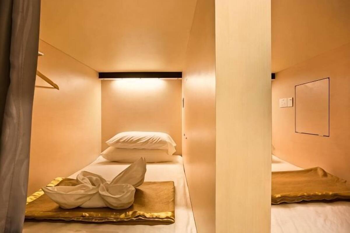 A small, cozy room with two beds, a wall-mounted light, and a framed picture.
