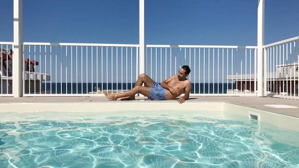 A man relaxing by a pool with a clear view of the ocean. - Residence Ten Suite (Rimini)