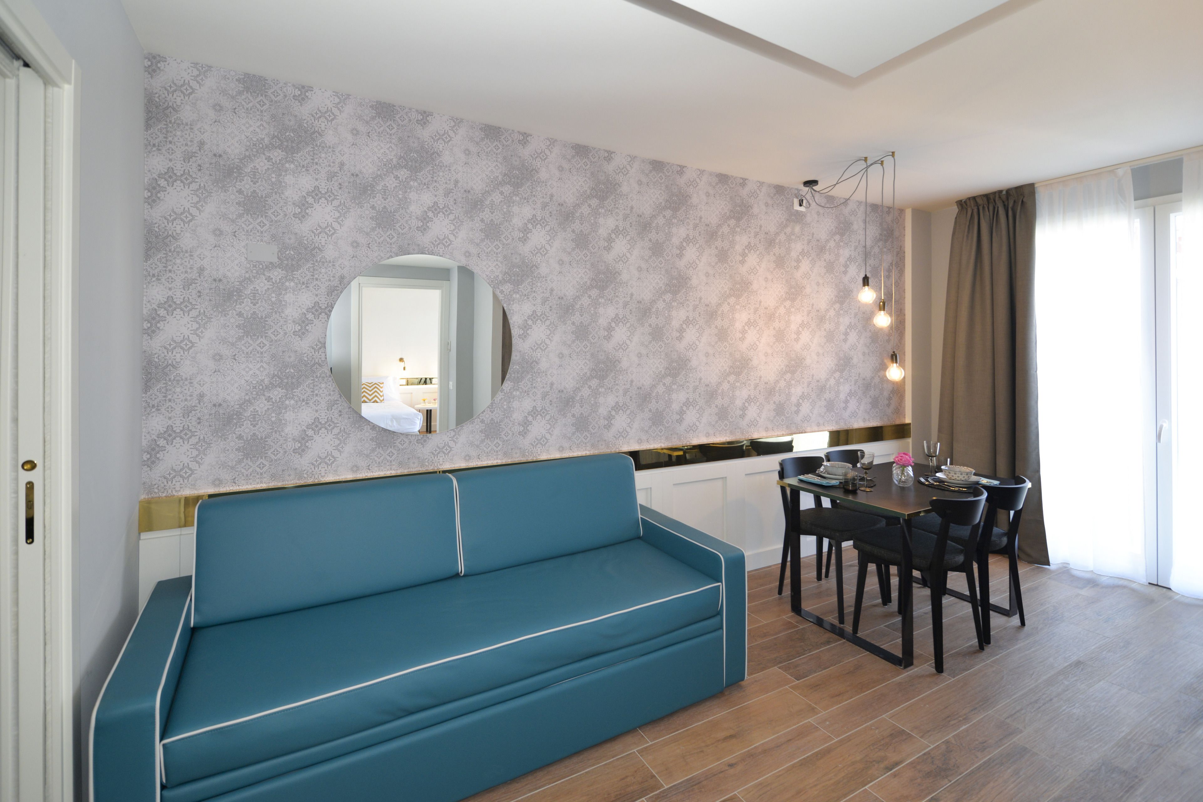 Een moderne woonkamer met een turquoise bank, een eettafel met stoelen en een behangen wand.
