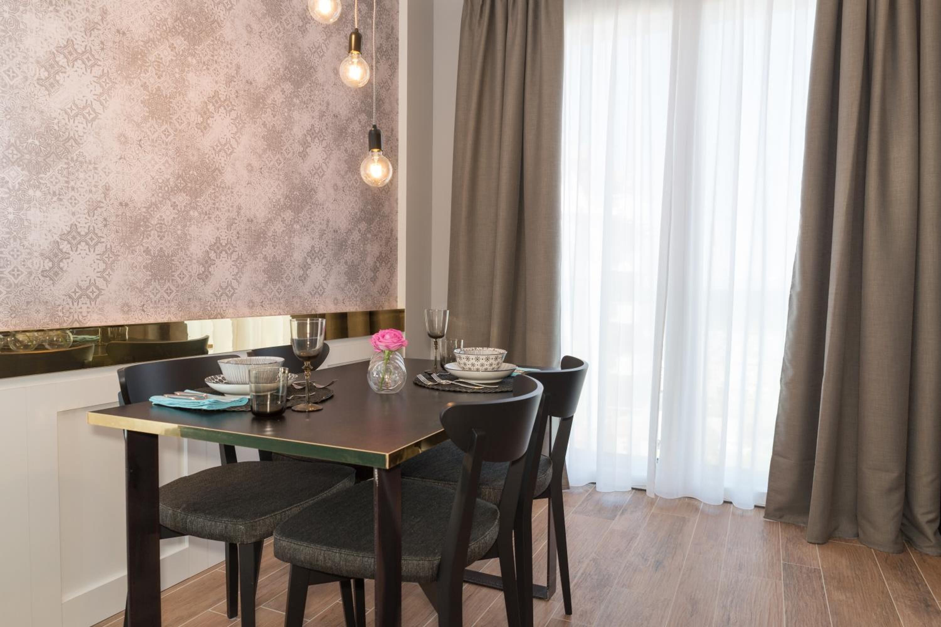 A dining area with a table set for four, chairs, a vase with a flower, and a patterned wall.