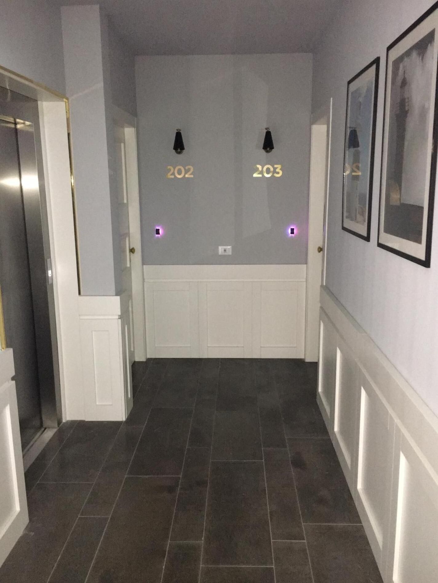 A hallway with dark tiled flooring, white wainscoting, and doors numbered 202 and 203.