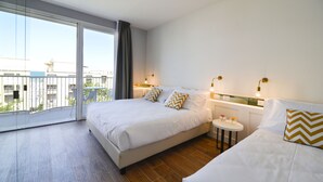 A hotel room with a large bed, a small bedside table, a chair, and a balcony with a view of buildings. - Residence Ten Suite (Rimini)