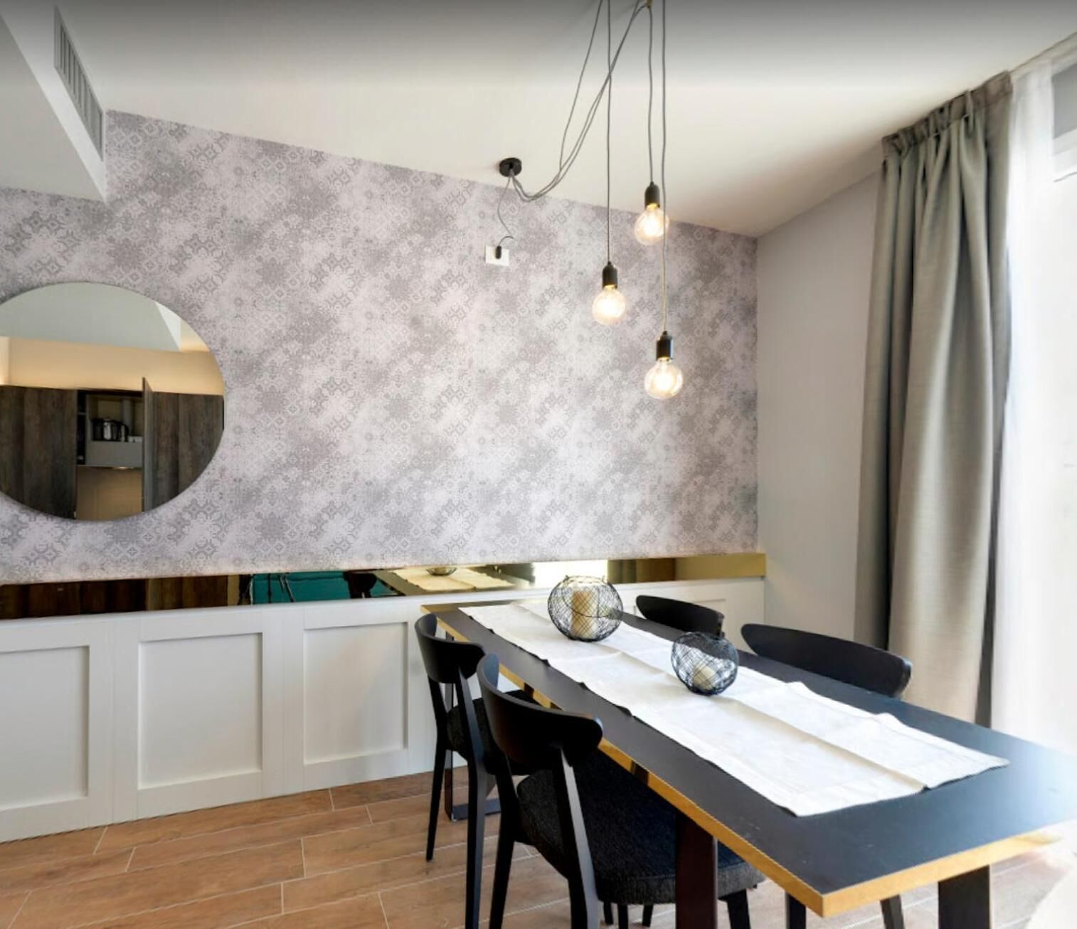 Une cuisine moderne avec un mur arrière décoré de motifs, un miroir rond et des luminaires suspendus.
