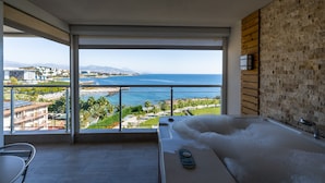 A modern bathroom with a large bathtub, a view of the sea, and a balcony with a cityscape in the background. - Adenya Hotel & Resort (Alanya)