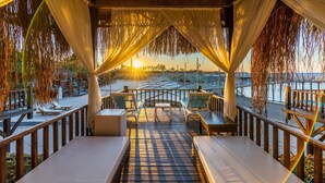 An outdoor seating area with tables and chairs, a wooden deck, and a view of the sunset over the water. - Adenya Hotel & Resort (Alanya)