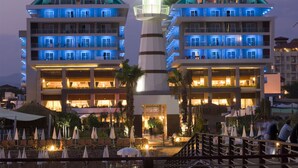 A hotel with multiple floors, a central tower, and outdoor seating areas with umbrellas. - Adenya Hotel & Resort (Alanya)