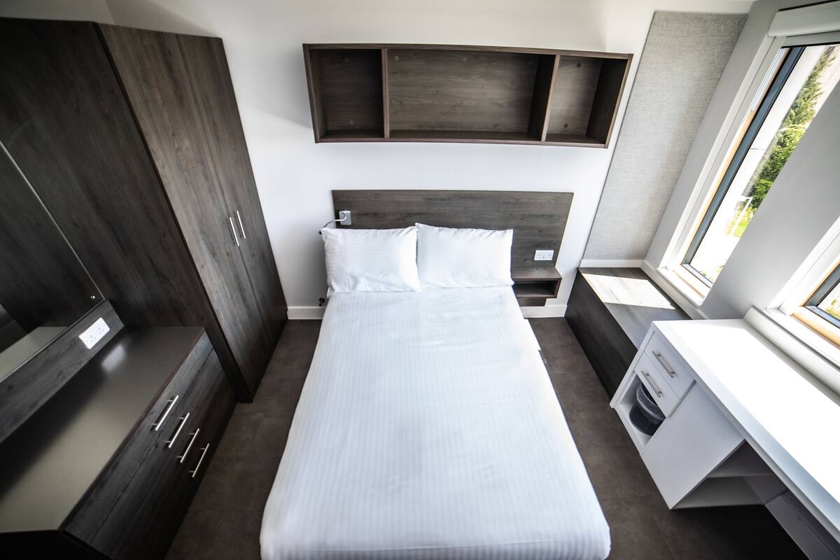 A modern bedroom with a large bed, built-in wardrobe, and a desk with storage.