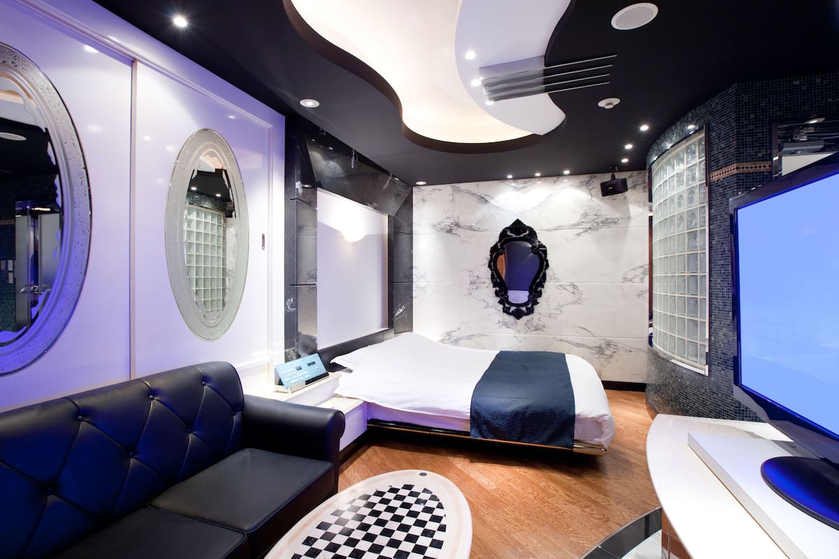 Una habitación de hotel moderna con una cama, un sofá, un televisor y un tapete de piso con un estampado de cuadros original.