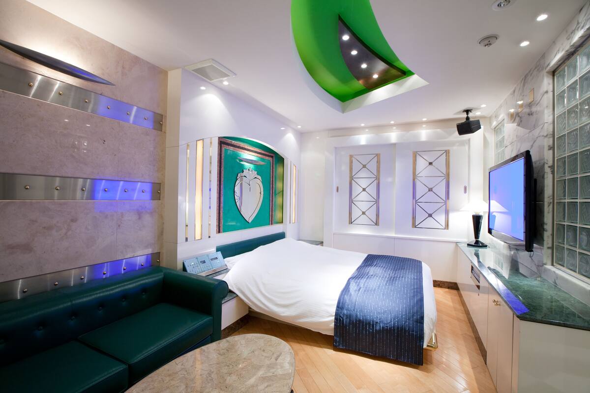 Una habitación de hotel moderna con cama, sofá verde y televisor.