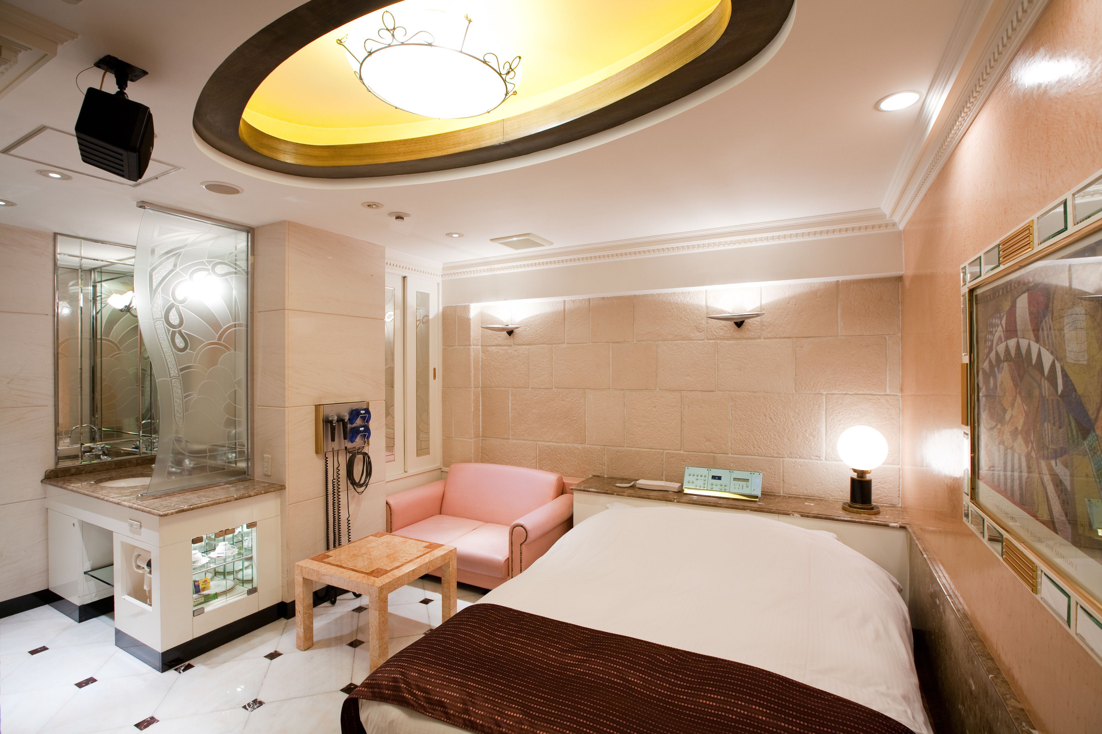 A hotel room with a bed, a chair, a small table, a mirror, and a wall-mounted clock.