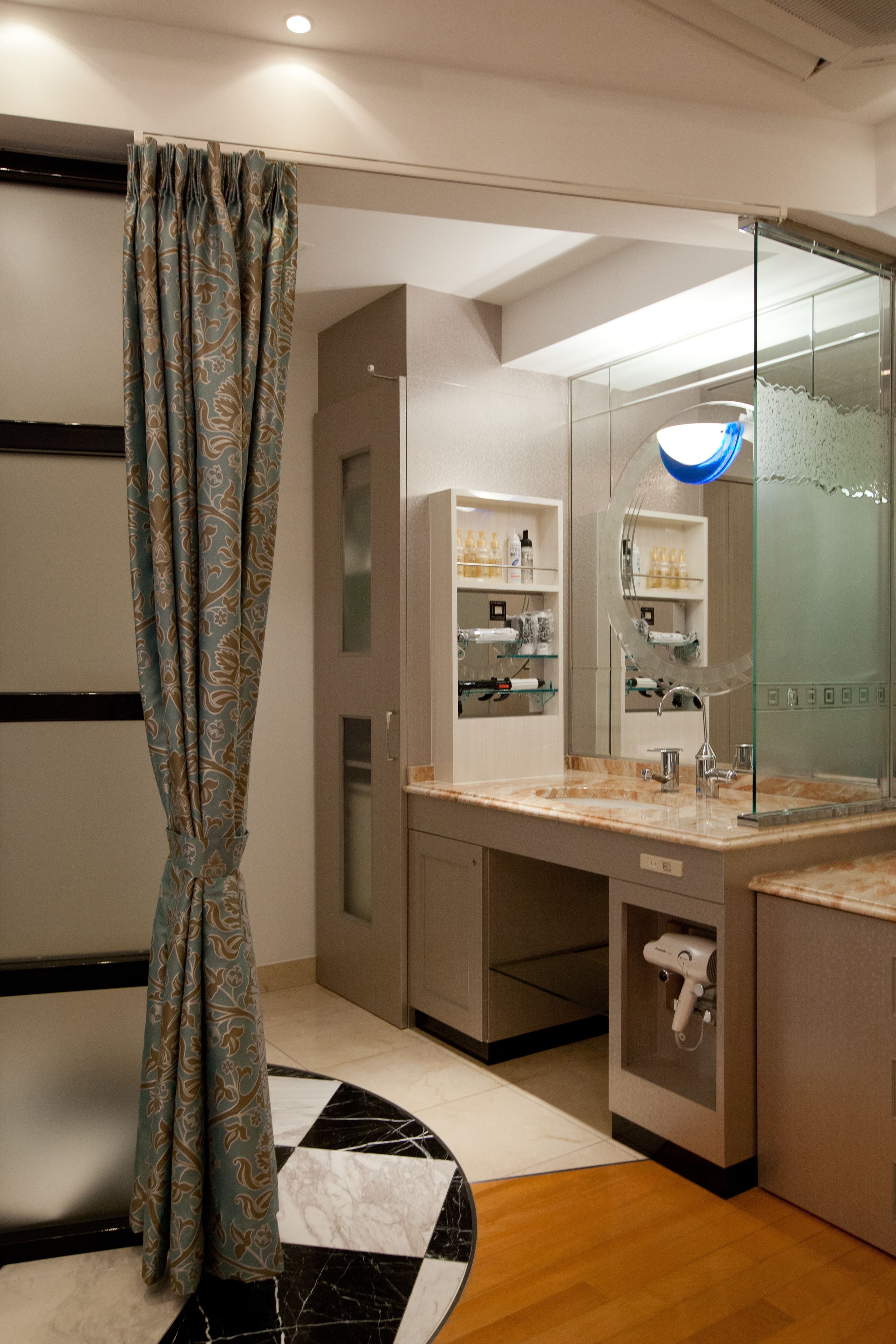 A modern bathroom with a shower curtain, a glass-enclosed vanity, and a marble-tiled floor.