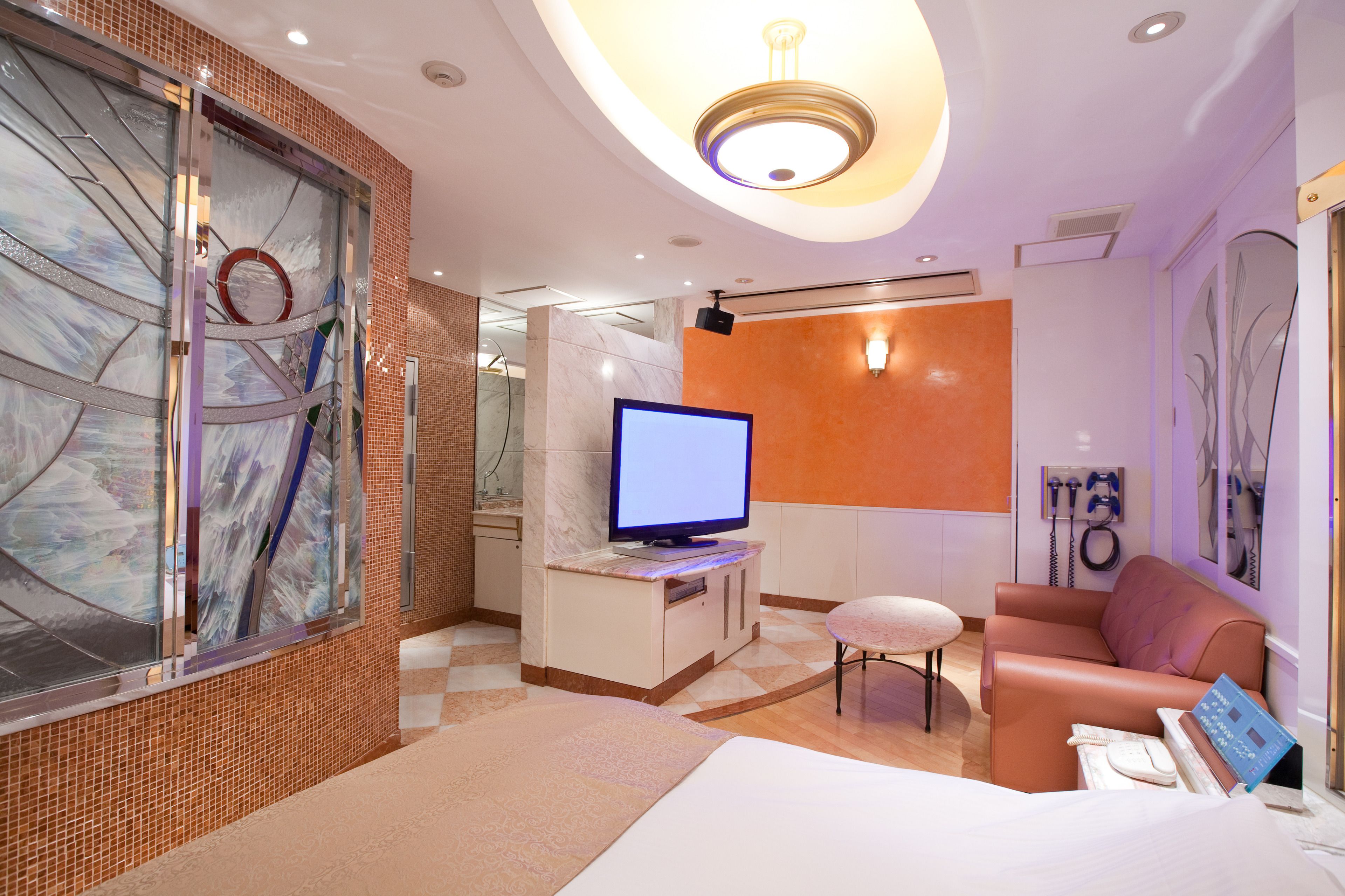 Habitación de hotel con cama, televisor, zona de estar y baño visible a través de un separador de vidrio.