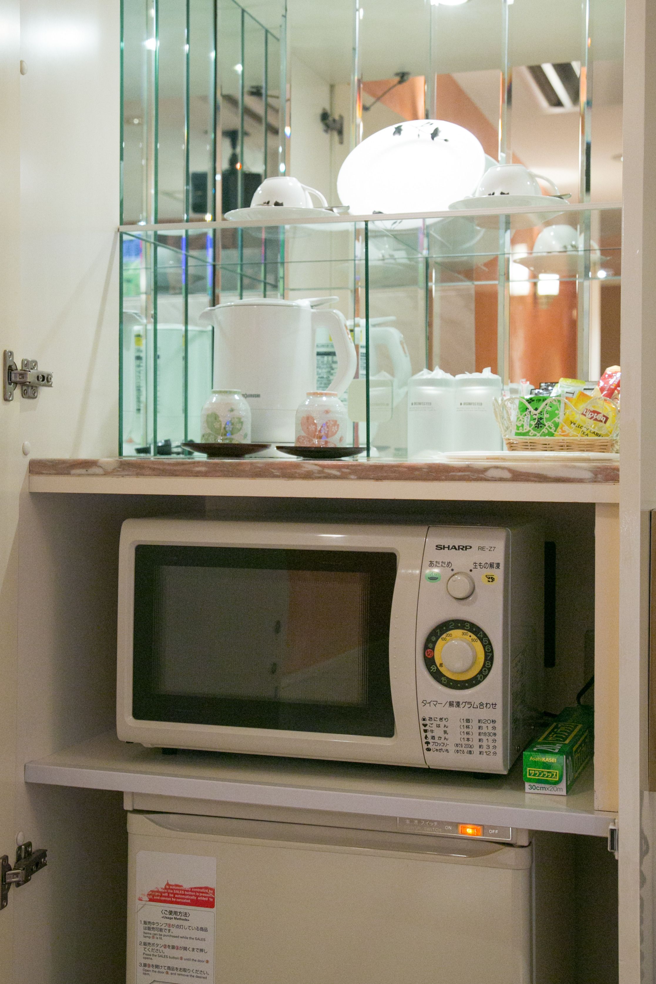 A microwave on a shelf above a cabinet, with a glass display case containing various items.