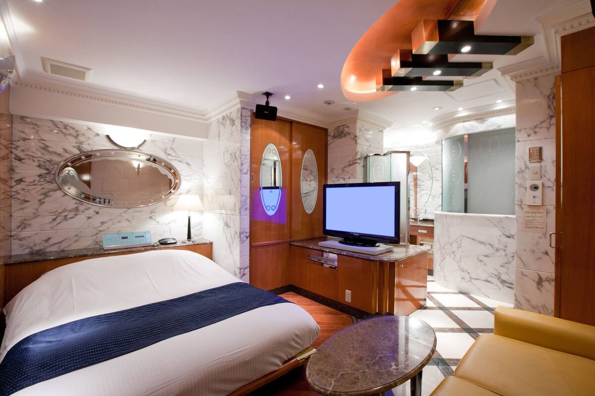 Habitación de hotel con una cama grande, televisión, escritorio con computadora, espejo y una mesita.