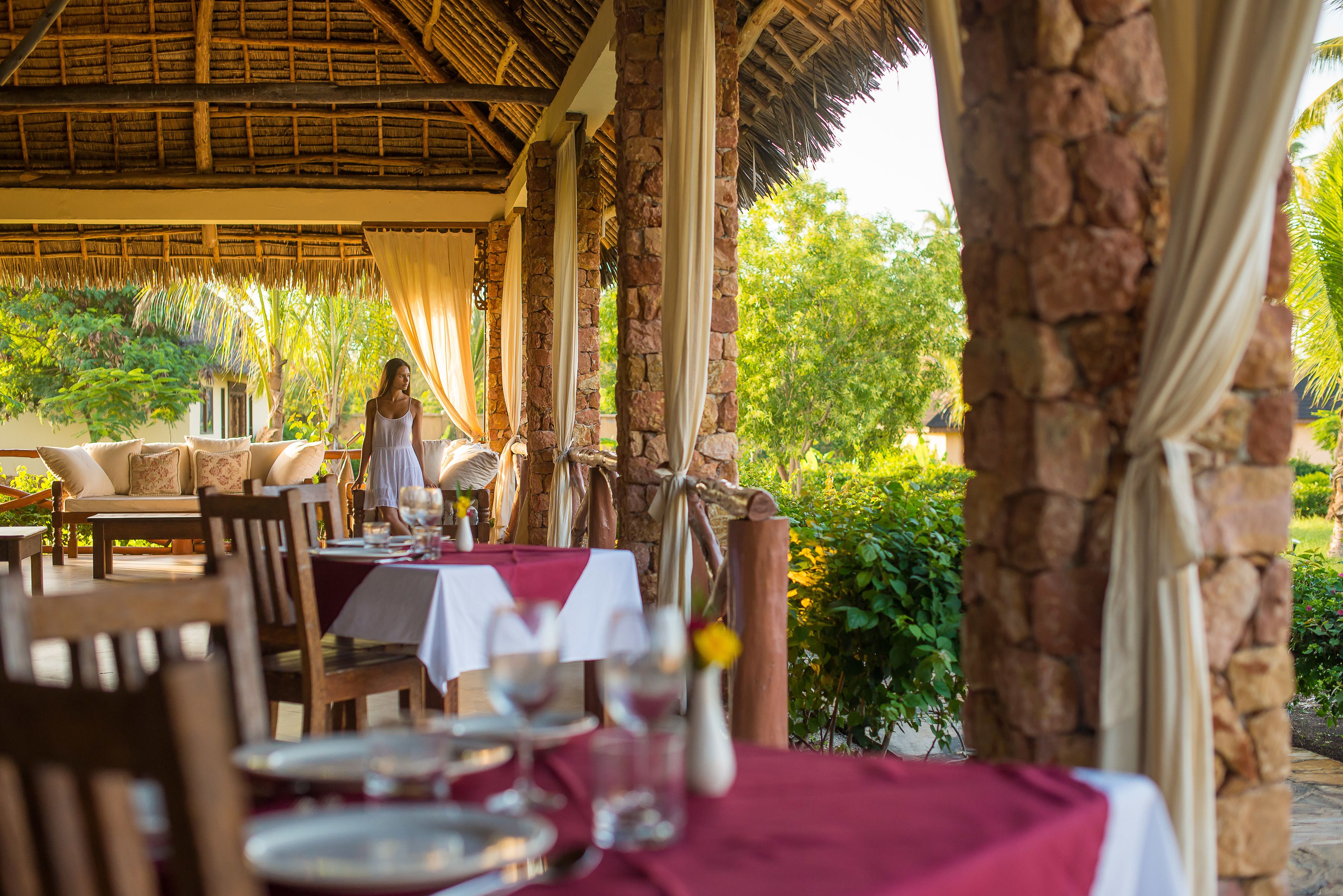 An outdoor dining area with stone pillars, wooden furniture, and tables set for a meal.