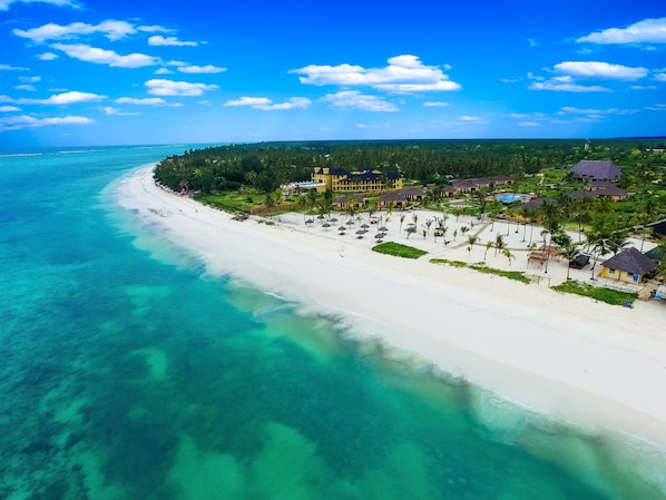 An aerial view of a beach resort with white sand, clear turquoise water, and a line of palm trees. - The Sands Beach Resort Zanzibar (Dongwe)