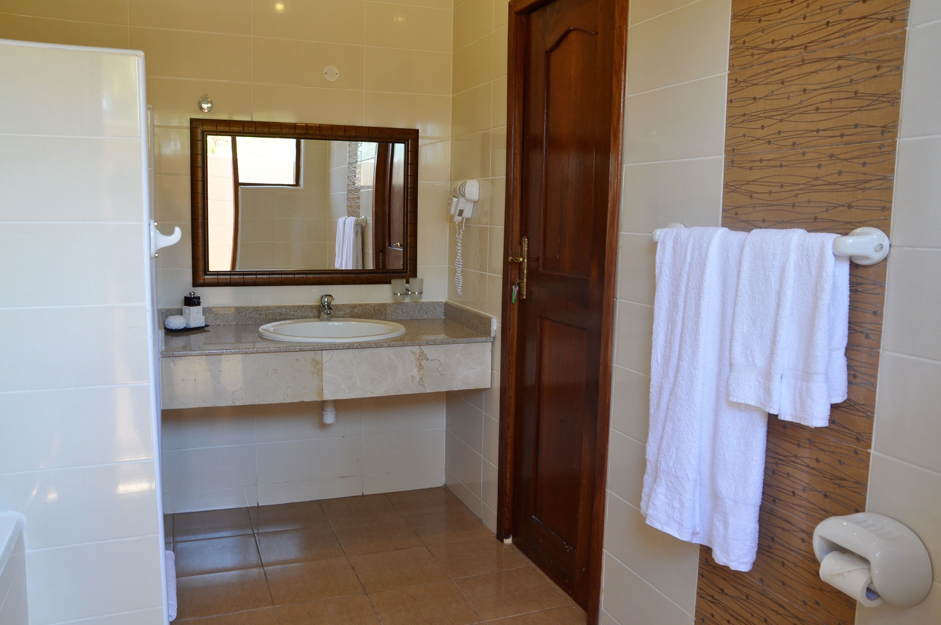 Un baño con lavamanos, espejo, toallero y puerta de madera.