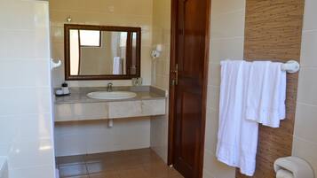 Un baño con lavamanos, espejo, toallero y puerta de madera.