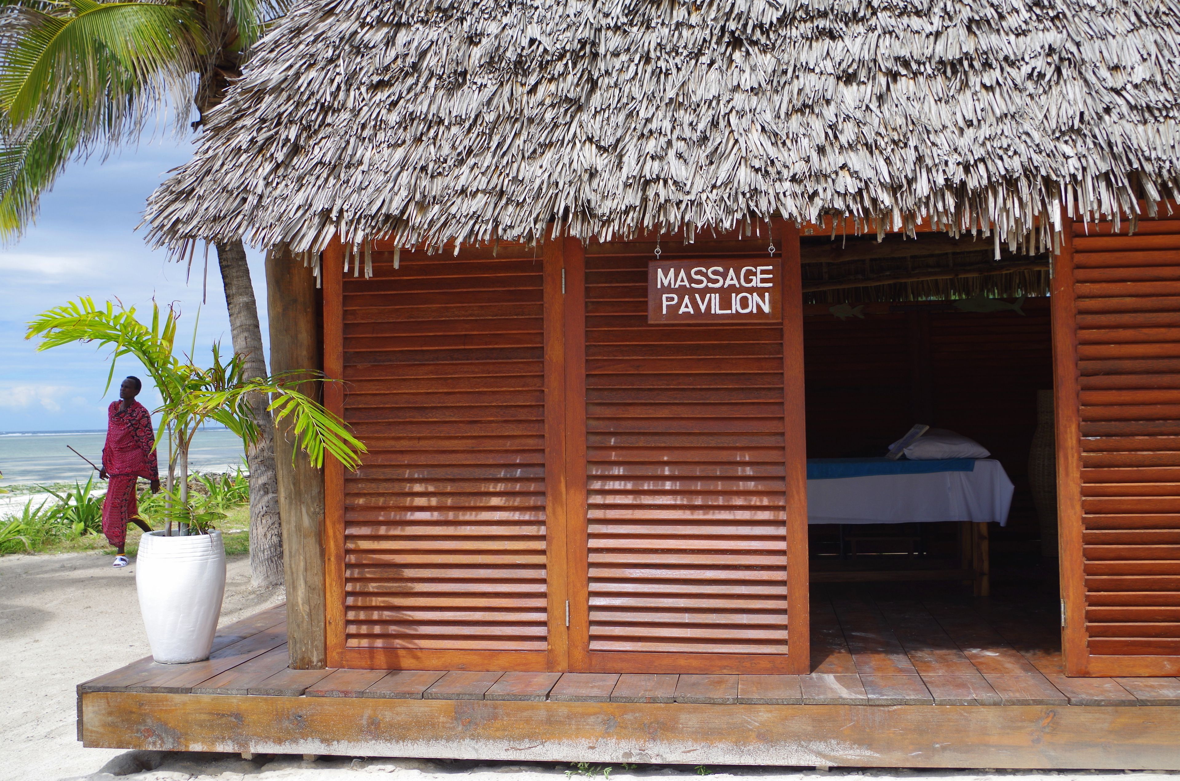 A massage pavilion with a thatched roof, wooden shutters, and a sign indicating its purpose.