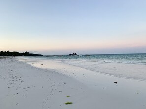 A beach with white sand, calm water, and a pier with overwater bungalows.
