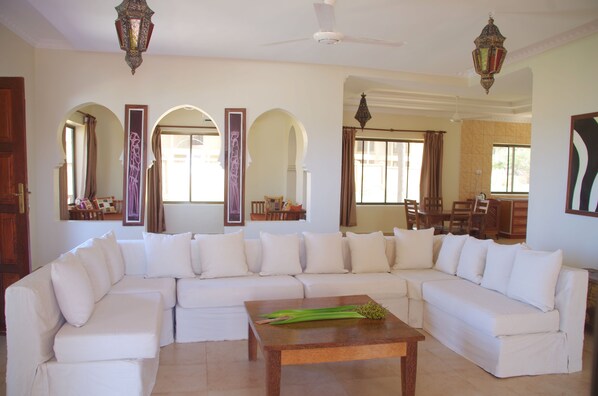 A spacious living room with a large white sectional sofa, a wooden coffee table, and decorative lanterns. - The Sands Beach Resort Zanzibar (Dongwe)