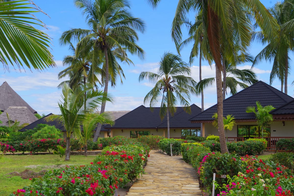 Ein Resort mit mehreren Gebäuden, einem Steinweg und üppiger Vegetation, darunter Palmen und blühende Pflanzen.