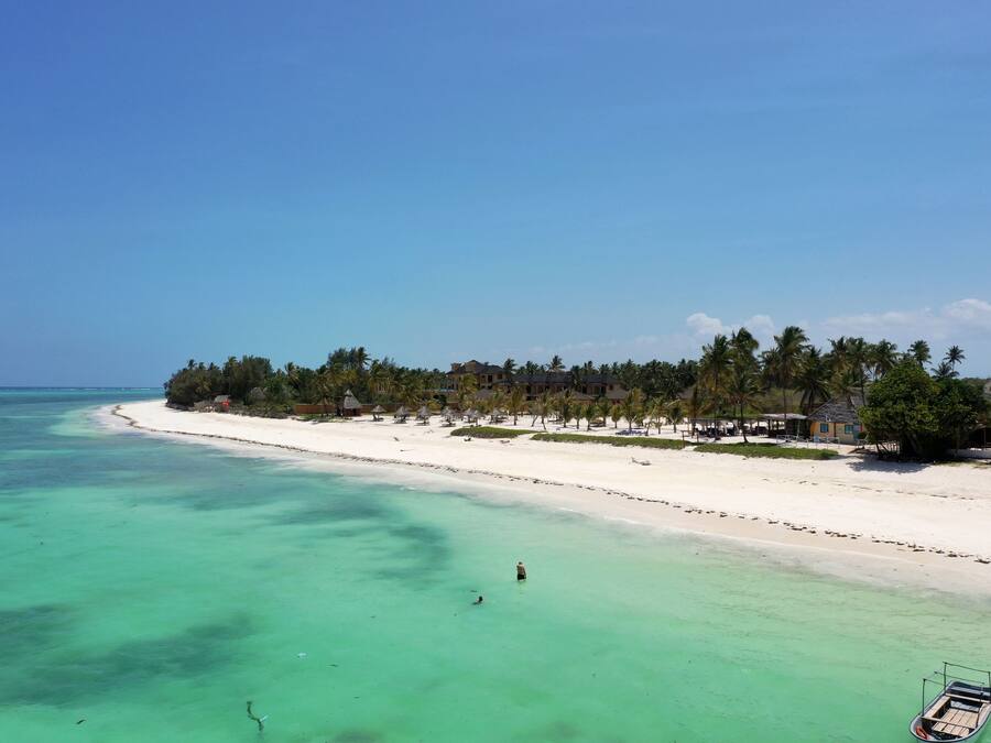 A beach resort with a white sandy shore, clear turquoise water, and a row of palm trees.