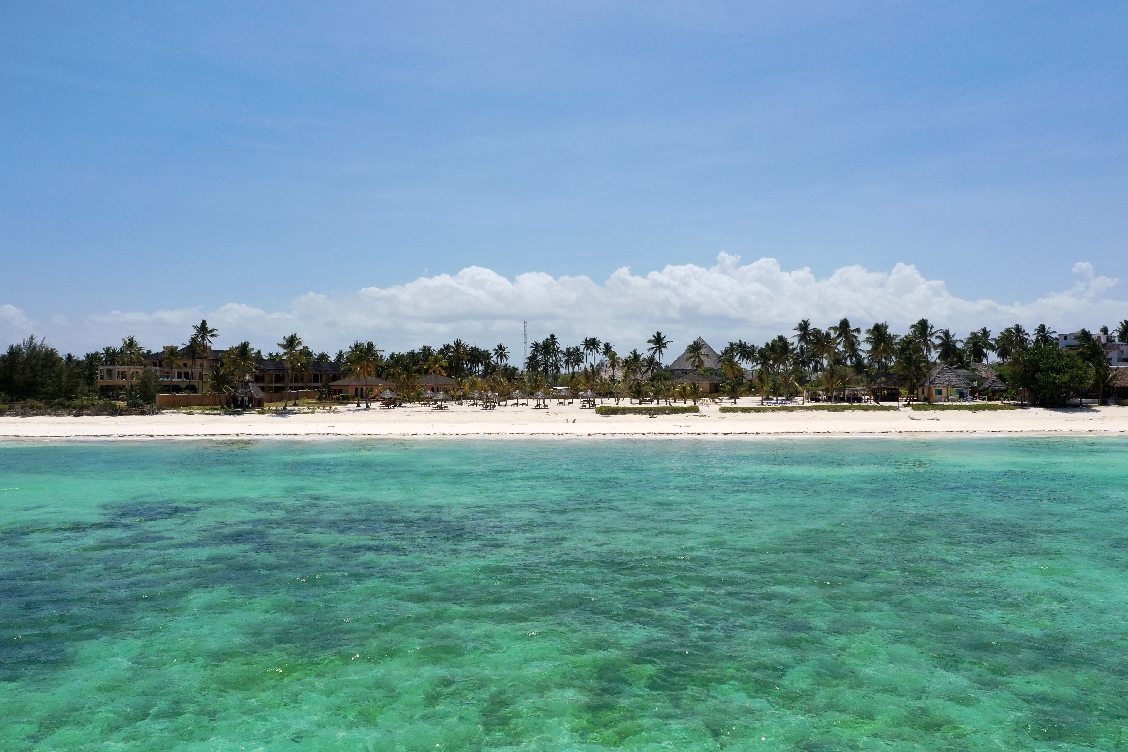 Un complejo turístico en la playa con aguas turquesas cristalinas, arena blanca y palmeras.