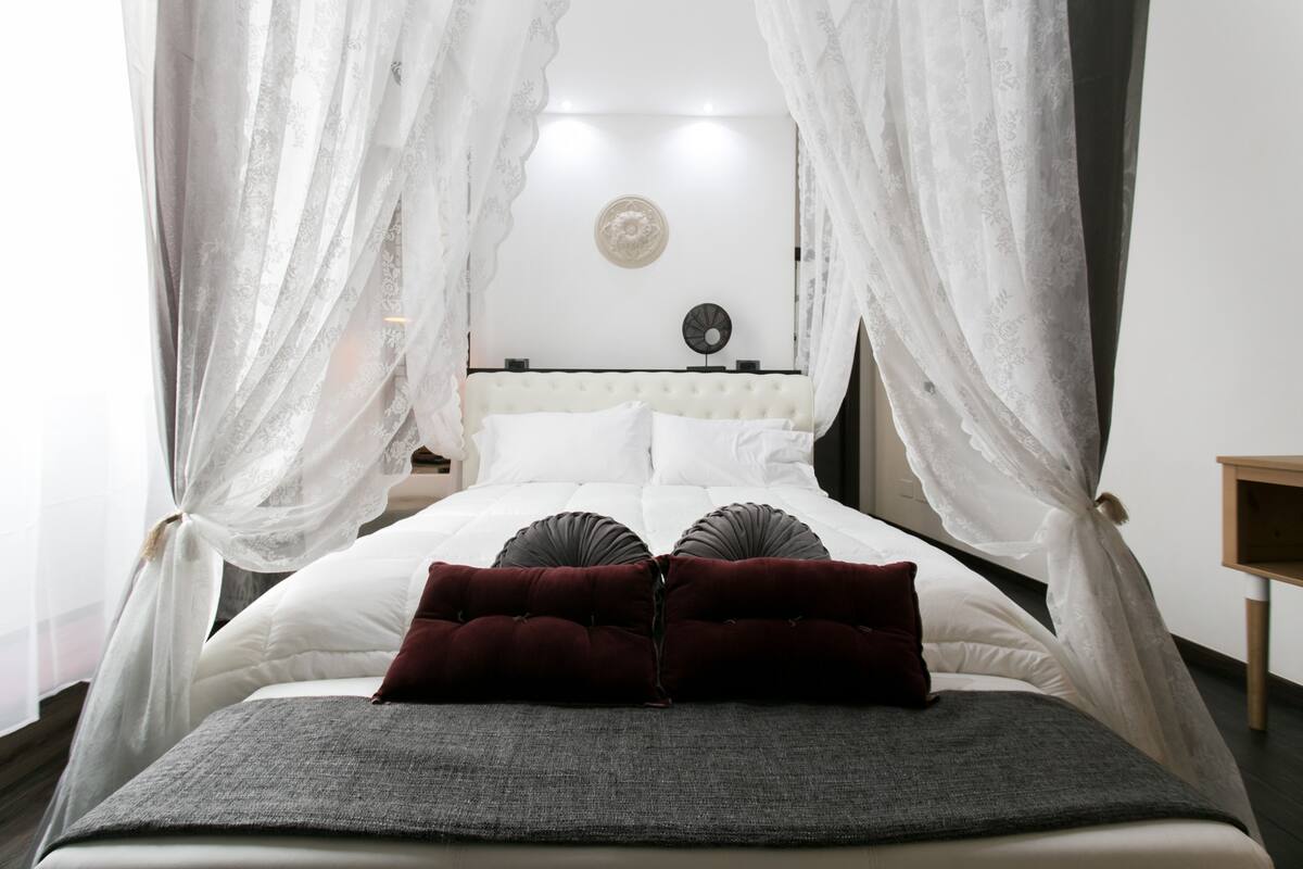A bed with white bedding, red pillows, and a grey throw blanket.