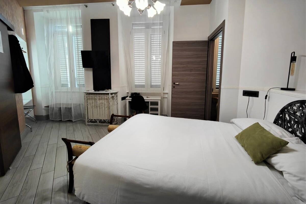A bedroom with a large bed, a desk, a chair, a wardrobe, and a TV.