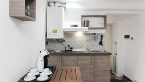A compact kitchen with a coffee machine, a kettle, and a small table with cups. - Aparthotel dei Mercanti (Milan)