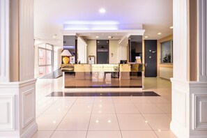 A hotel lobby with a reception desk, a large lamp, and a cross on the wall.
