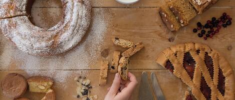Une table en bois sur laquelle sont disposés divers produits de boulangerie, notamment un gâteau en forme de couronne, des biscuits et une tarte, ainsi qu’un bol de yaourt et un couteau.