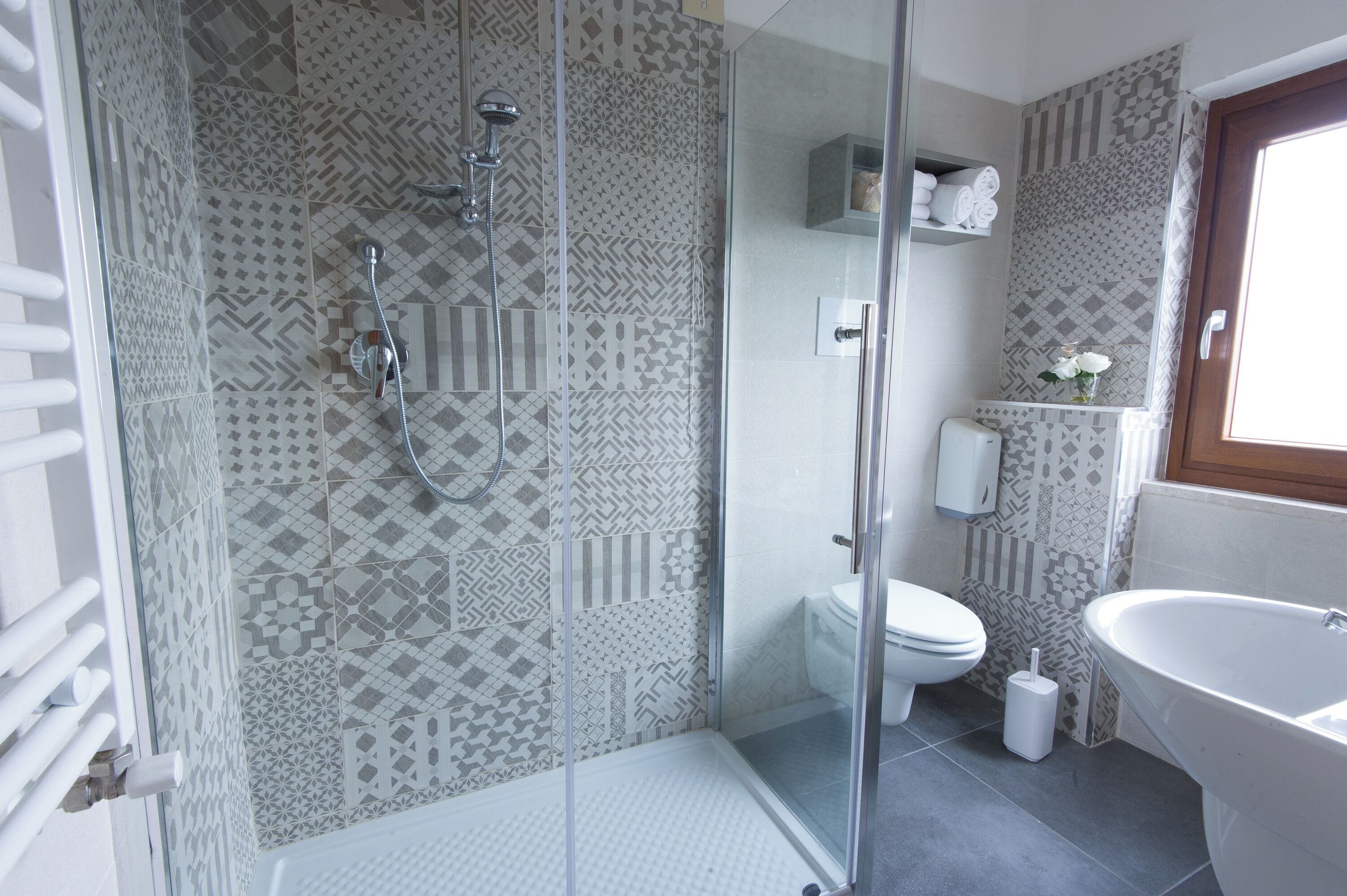 Un baño moderno con baldosas estampadas, una ducha con mampara de vidrio, un inodoro, un lavamanos y una bañera.