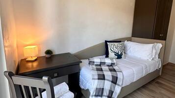 Een kleine, verzorgde slaapkamer met een enkel bed, een nachtkastje met lamp, een stoel en een garderobe.