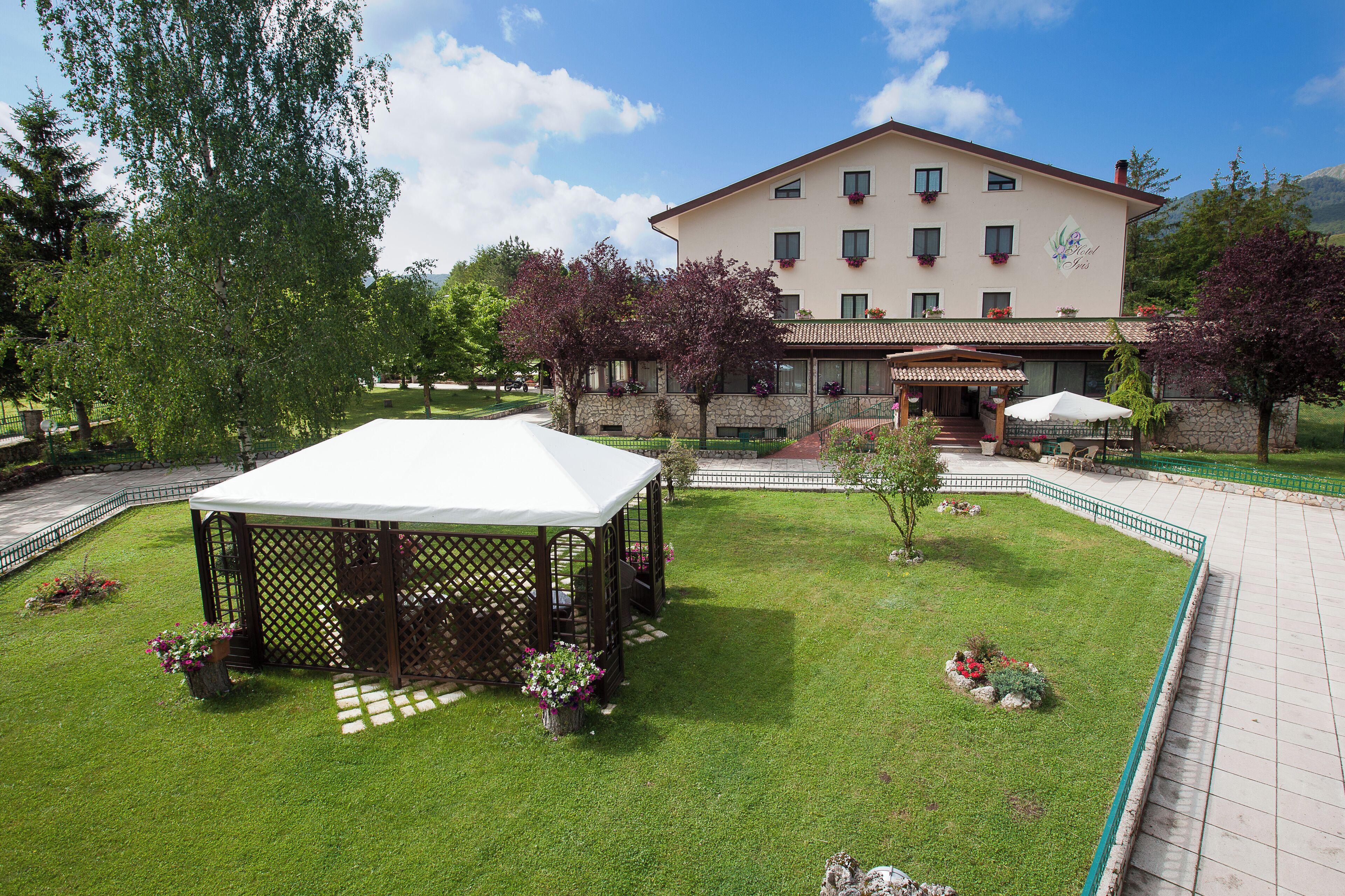 A hotel with a covered outdoor seating area, a stone facade, and a well-maintained lawn.