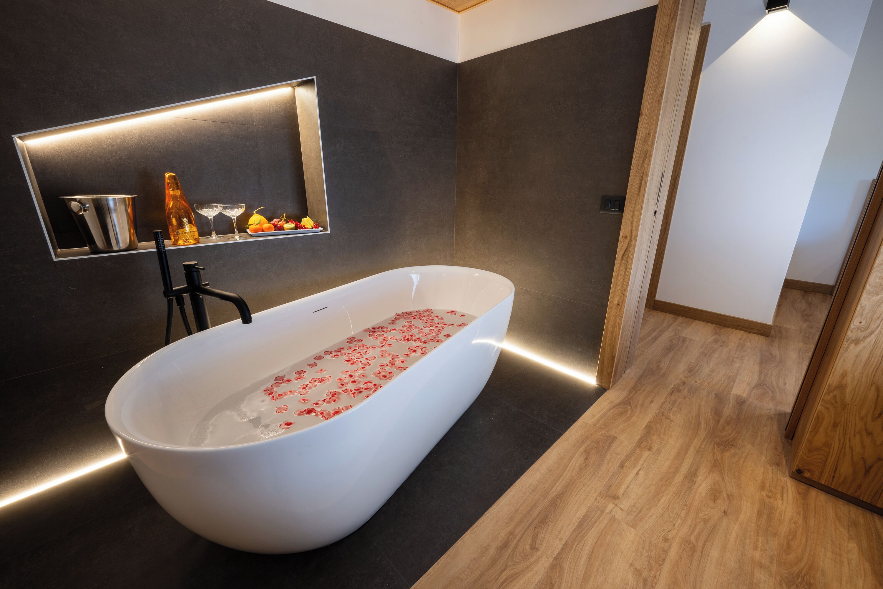 Ein modernes Badezimmer mit einer freistehenden Badewanne, einer integrierten Ablage mit Toilettenartikeln und einem Spiegel darüber.