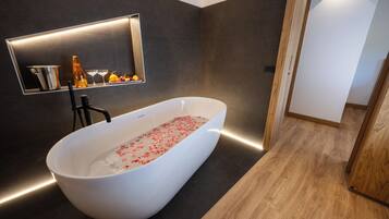 Ein modernes Badezimmer mit einer freistehenden Badewanne, einer integrierten Ablage mit Toilettenartikeln und einem Spiegel darüber.