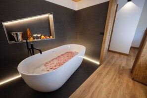A modern bathroom with a freestanding bathtub, a built-in shelf with toiletries, and a mirror above the shelf. - Hotel Iris (Pescasseroli)