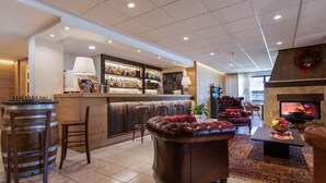 A bar area with stools, a fireplace, and a seating area with a leather ottoman and chairs. - Hotel Iris (Pescasseroli)