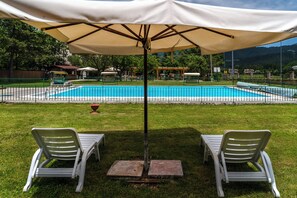 A pool area with two lounge chairs under a canopy, surrounded by a fence and greenery. - Hotel Iris (Pescasseroli)