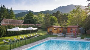 A swimming pool with lounge chairs, a bar, and cabins in a mountainous area. - Hotel Iris (Pescasseroli)