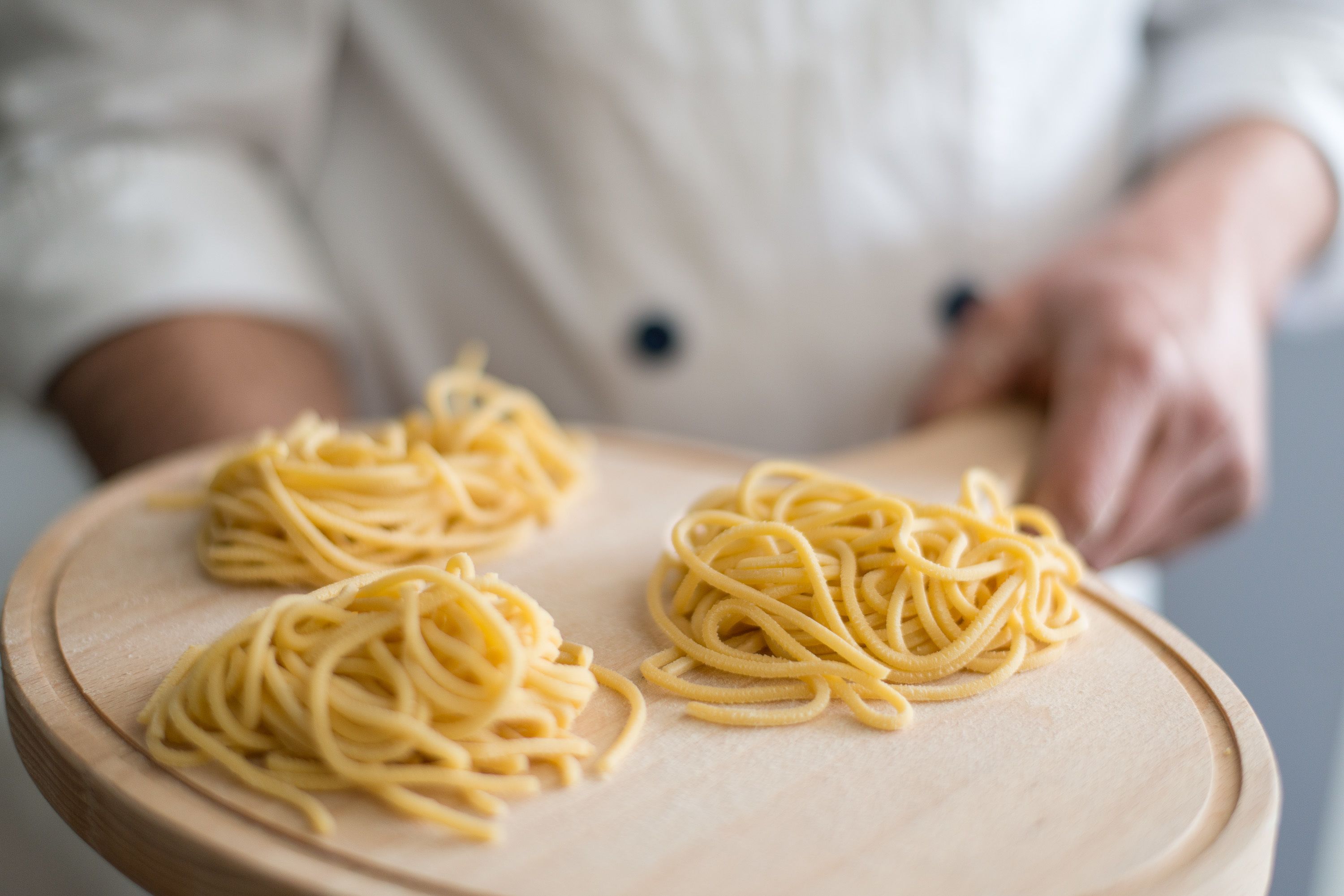 A chef's hands holding a wooden board with uncooked spaghetti.