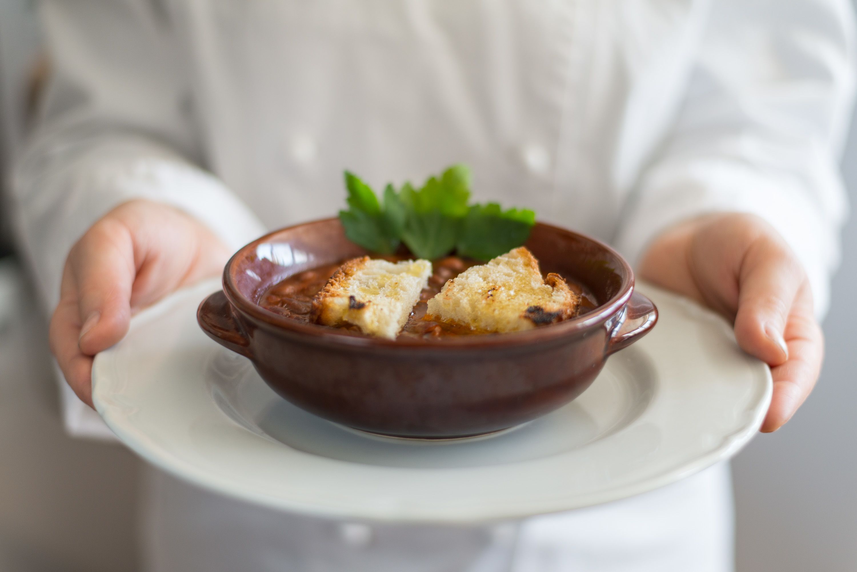 A person holding a ceramic dish with a food item and a garnish.