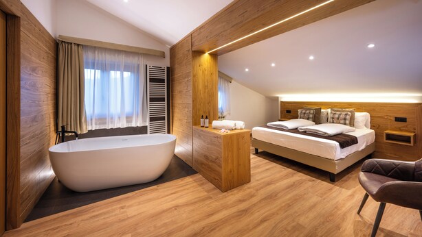 A modern bedroom with a large bathtub, a neatly made bed, and a wooden ceiling. - Hotel Iris (Pescasseroli)